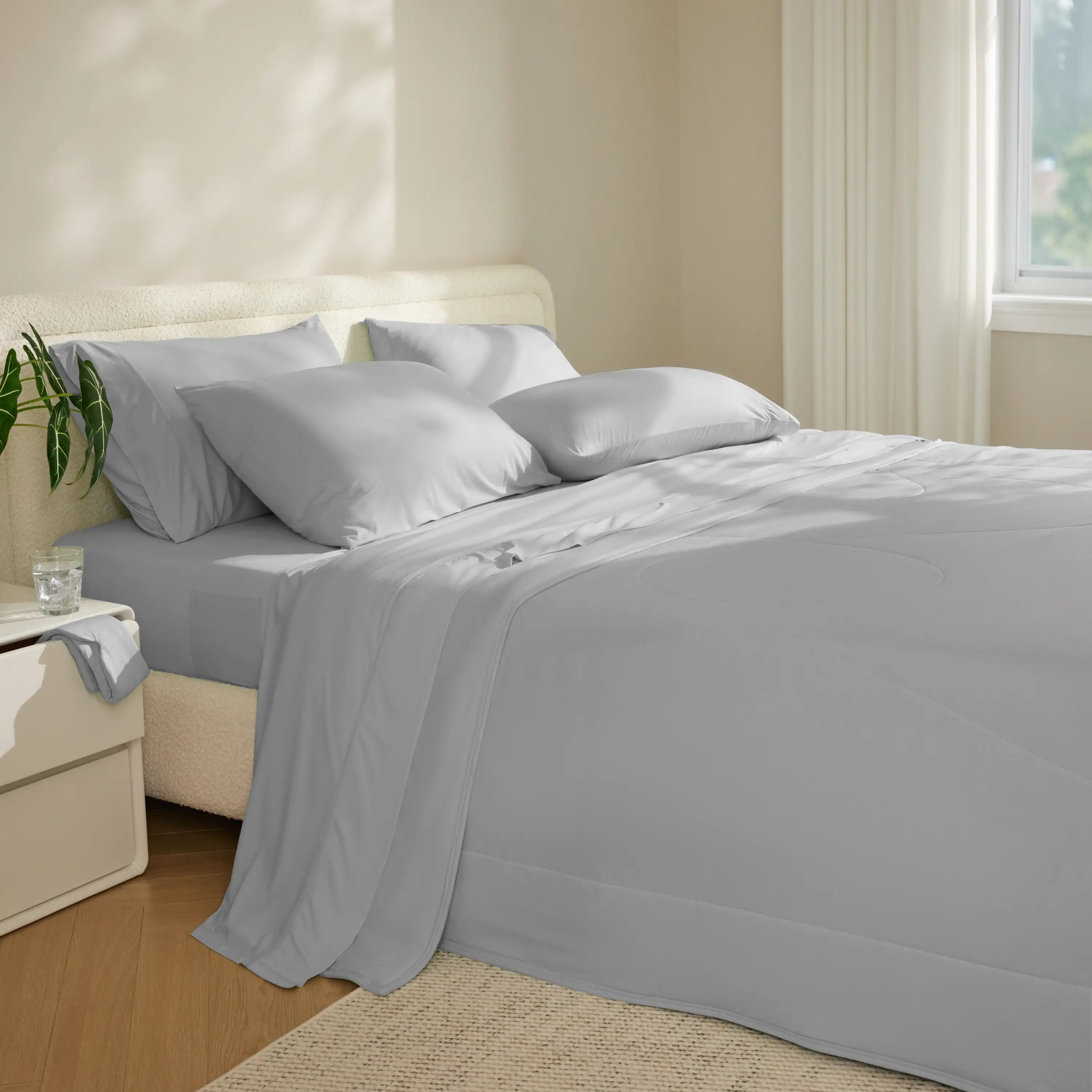 Gray bedding set on a bed in a bedroom with a nightstand and plant. #color_misty-grey