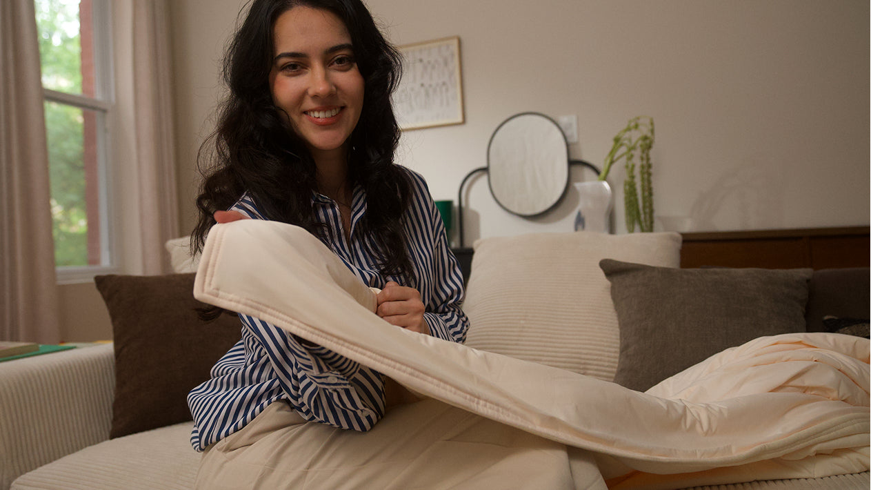 Woman sitting on a couch holding a folded blanket in a living room.