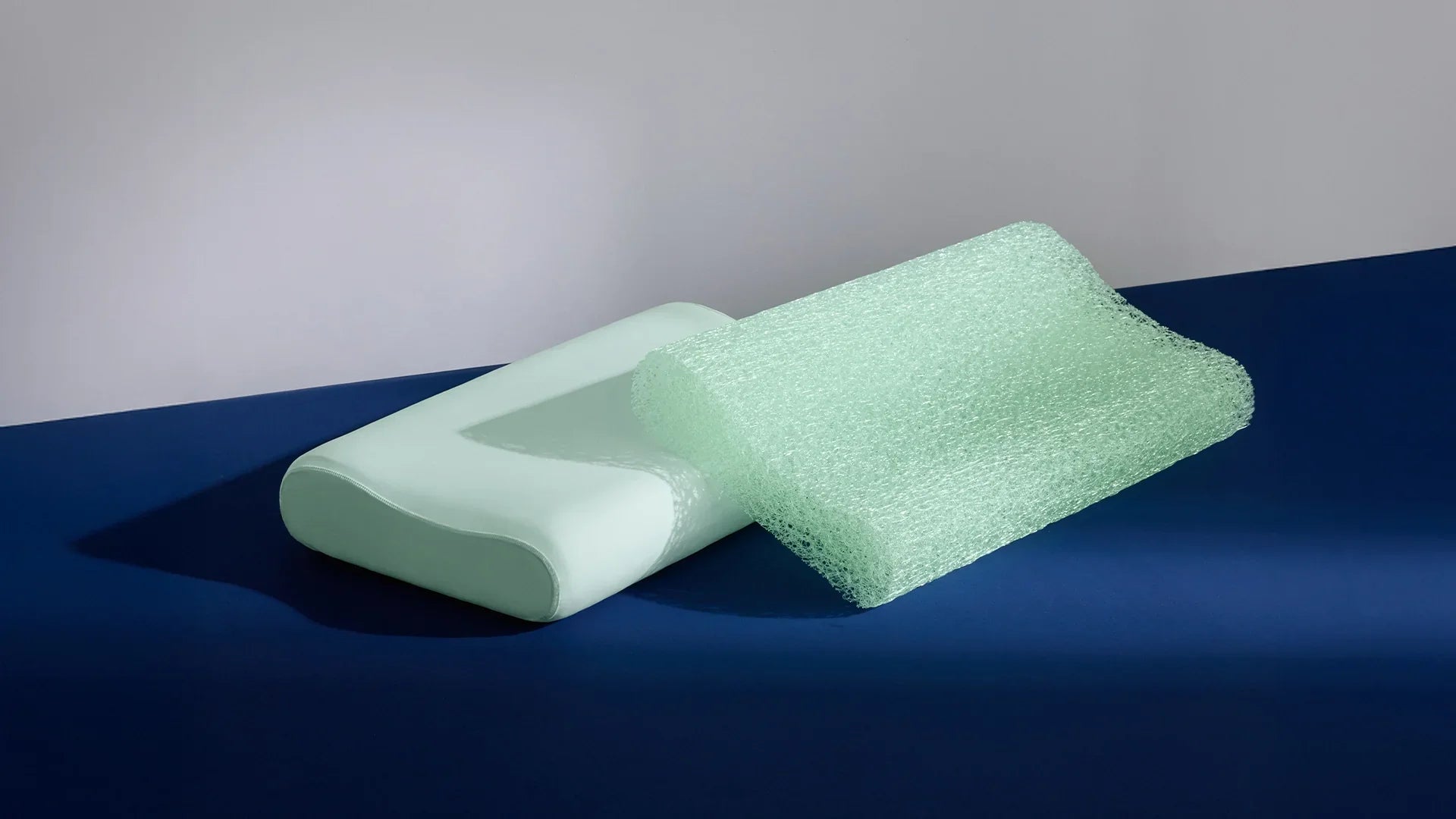 A smooth mint green contour pillow and a textured green mesh pillow resting side-by-side on a blue surface