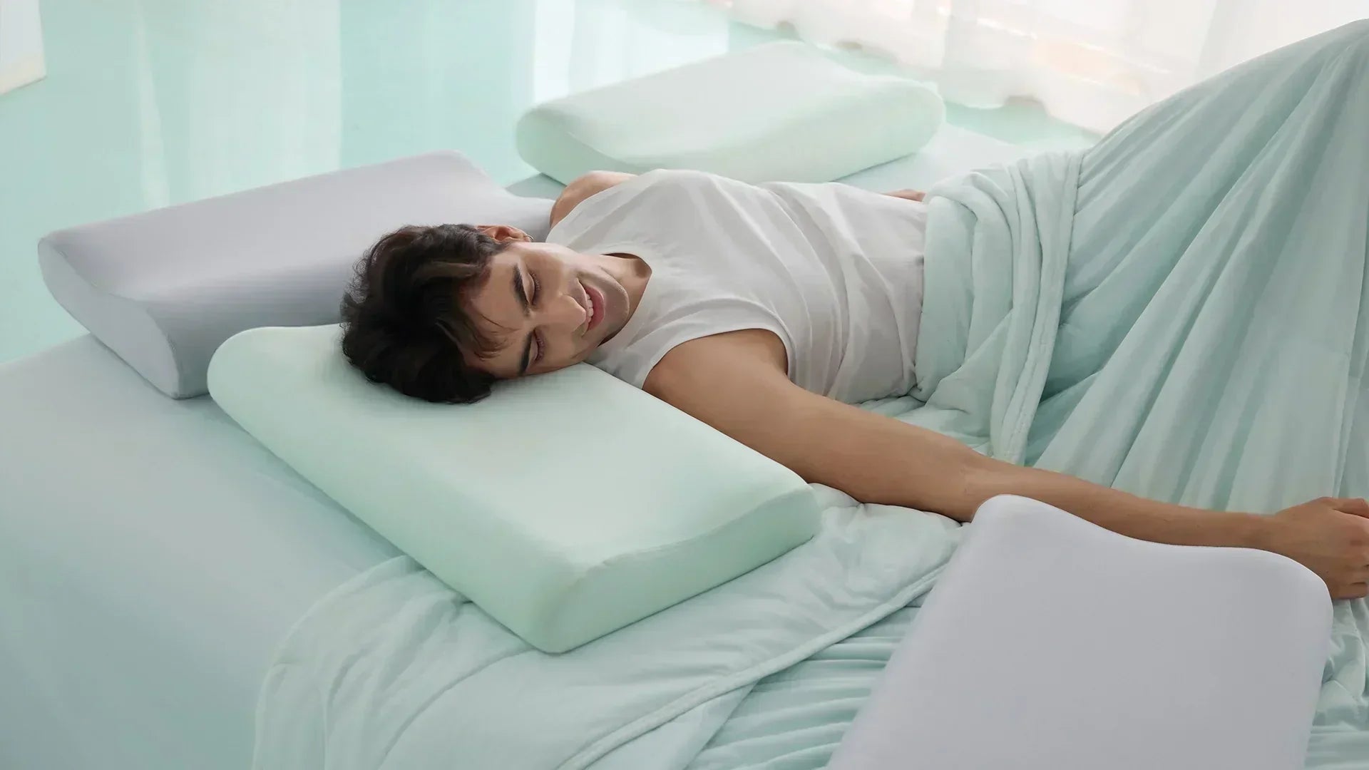 Man sleeping comfortably on mint green bedding with ergonomic memory foam pillows supporting his head and arm