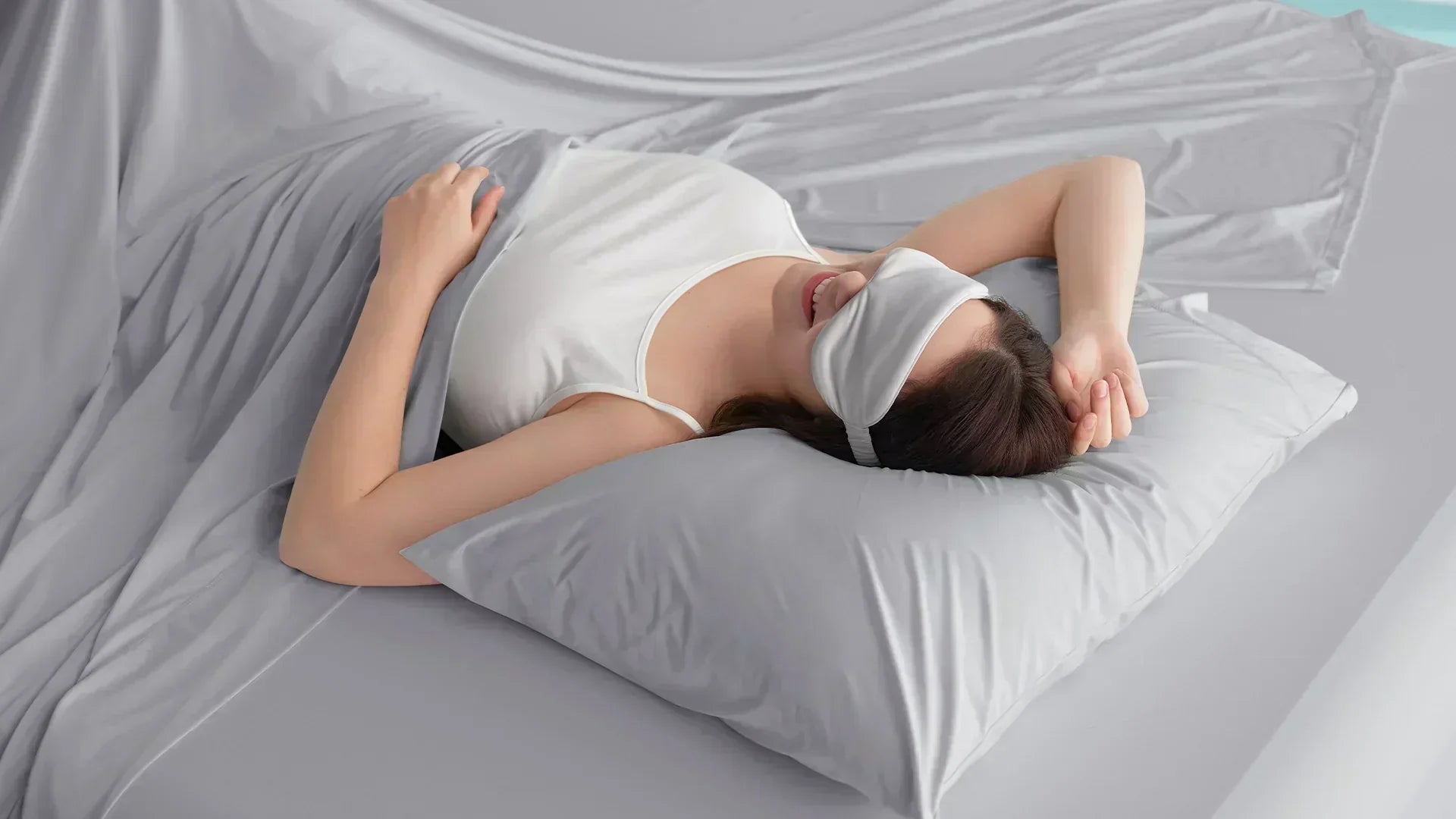 Woman sleeping comfortably with an eye mask under a grey cooling comforter