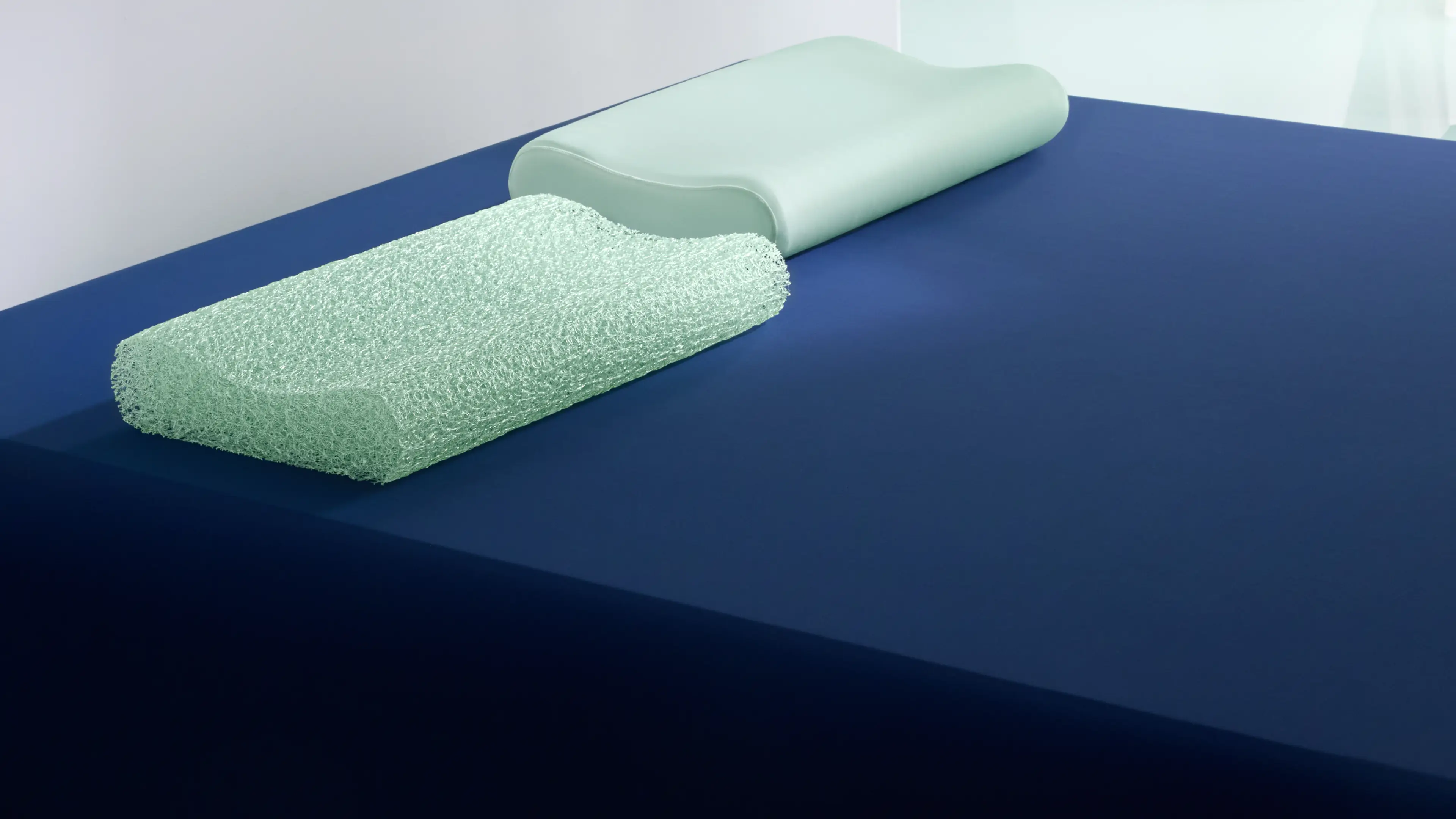 A smooth green cooling pillow and its exposed open-mesh core on a blue mattress