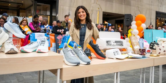 Woman standing behind a table displaying various sneakers with people in the background.