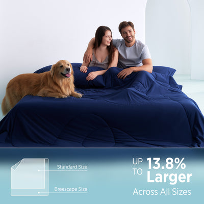 Couple and dog on twilight blue Breescape comforter, showing 'Up to 13.8% Larger' than standard.